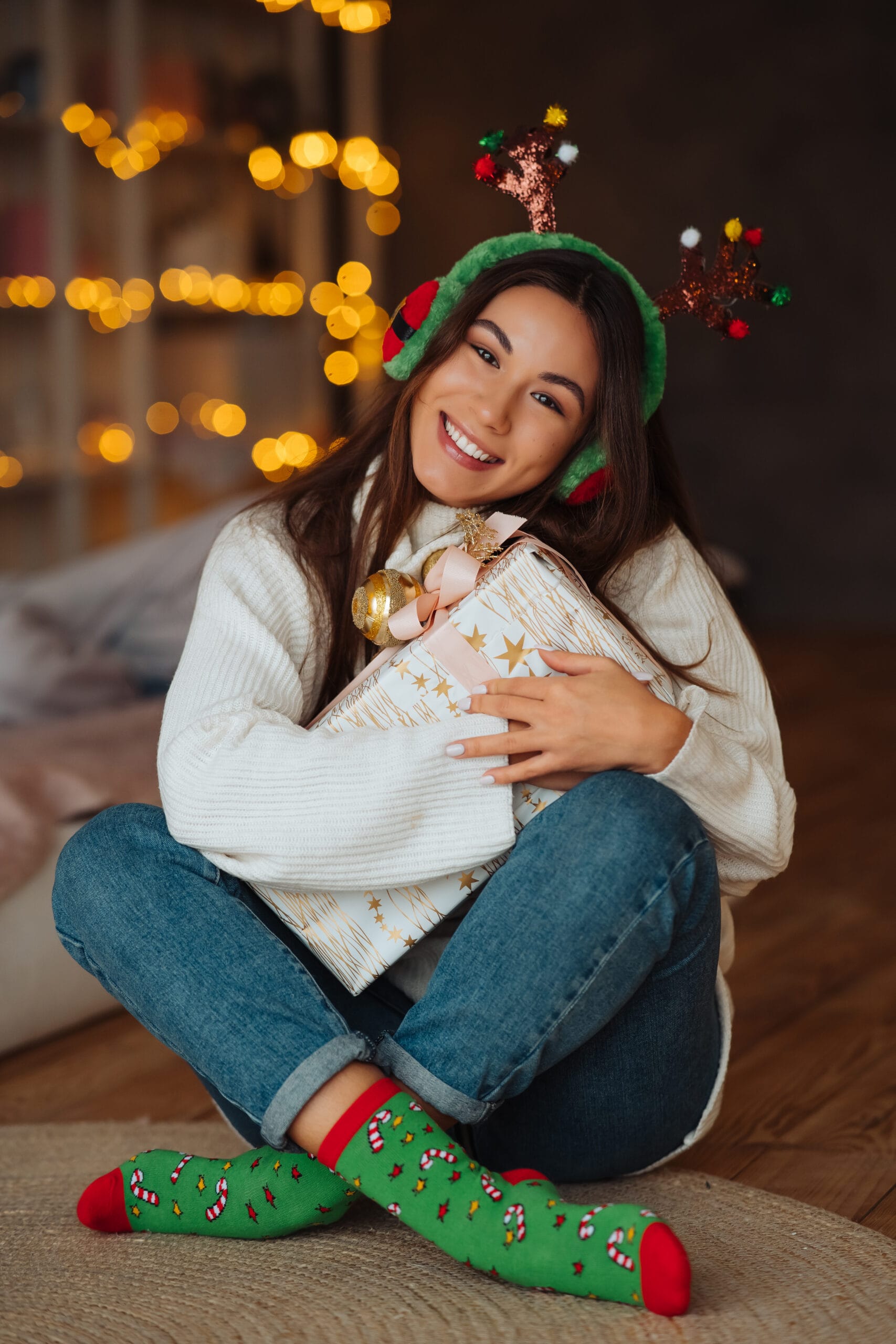 Girl close up with gift smiling to camera. She wearing christmas antlers.